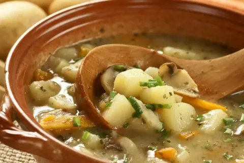 Zupa ziemniaczana przepis babci. Aromatyczna, domowa zupa z ziemniaków, marchewki i grzybów, podana w glinianej misce z drewnianą łyżką.