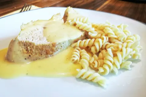 Kawałek pieczonego mięsa w kremowym sosie do potrawki, podany z makaronem fusilli.