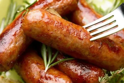 Soczysta kiełbasa z piekarnika, rumiana i aromatyczna, podana z gałązkami rozmarynu. Widok zachęca do spróbowania.