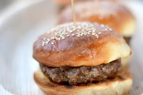 Mini burger z sezamową bułką i kotletem na talerzu.