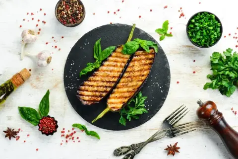 Grillowane bakłażany z bazylią i natką pietruszki. Idealne nietypowe dania z grilla, podane z czosnkiem, oliwą i pieprzem.