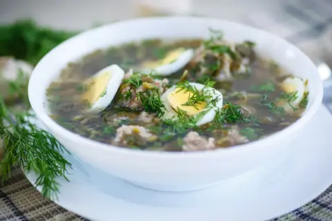 Zupa szczawiowa przepis babci: aromatyczna, zielona z dodatkiem mięsa i jajka, udekorowana świeżym koperkiem.