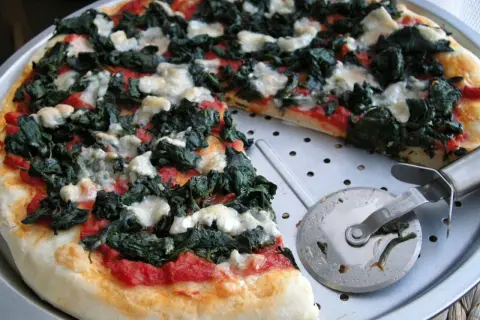 Pyszna pizza ze szpinakiem i białym serem, gotowa do pokrojenia.