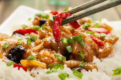Schab po chińsku z ryżem, posypany szczypiorkiem. Pałeczki podnoszą kawałek papryczki chili z aromatycznego dania.