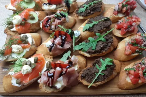 Tanie przekąski na imprezę: bruschetty z łososiem, szynką parmeńską, pastą z oliwek i pomidorami. Idealne na każdą okazję!
