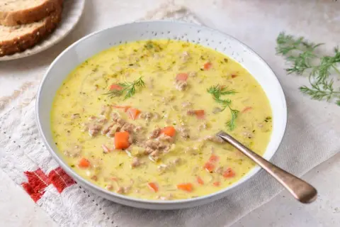 Gęsta zupa z pora z serkiem topionym i mięsem mielonym, ozdobiona koperkiem. Obok kromki chleba.