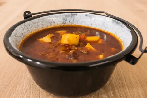 Gęsta, aromatyczna zupa gulaszowa przepis babci, z kawałkami mięsa i ziemniaków w głębokim, glinianym garnku.