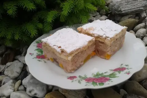 Dwa kawałki ciasta z kisielem na oleju, posypane cukrem pudrem, na talerzyku z różami, wśród kamieni i gałązek choinki.