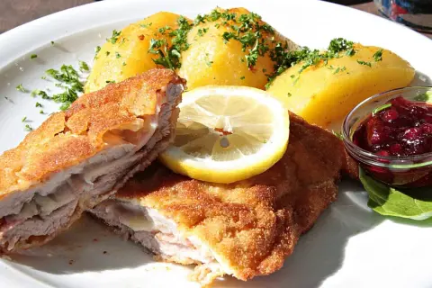 Pyszny kotlet po szwajcarsku, podany z ziemniakami, plasterkiem cytryny i żurawiną.