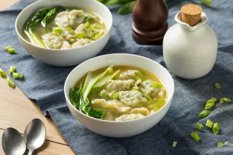 Dwie miseczki aromatycznej zupy won ton z zielonymi warzywami i posiekanym szczypiorkiem.