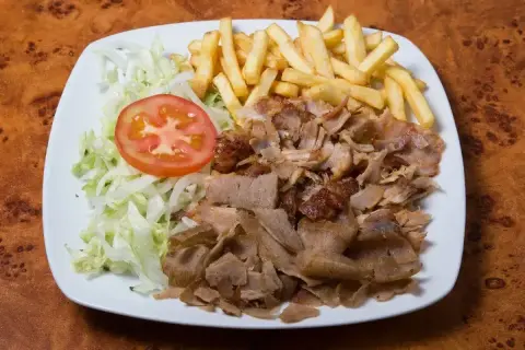 Talerz z prawdziwym kebabem, frytkami, sałatą i pomidorem. Apetyczny posiłek na drewnianym blacie.