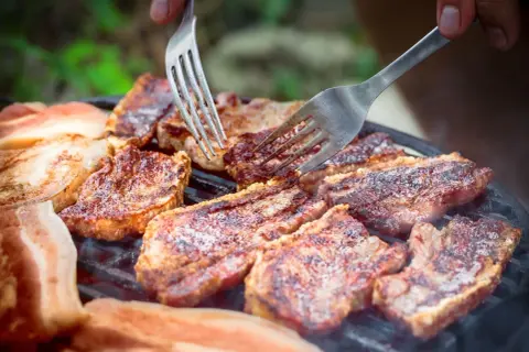 Soczysty boczek na grillu, idealny po marynacie. Dwie widelce sprawdzają stopień wysmażenia.