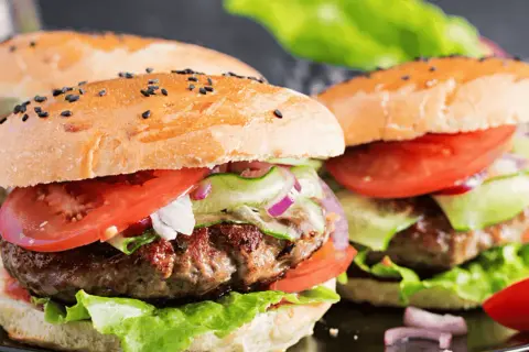 Dwa soczyste burgery wołowe z bułką, pomidorem, sałatą i ogórkiem.