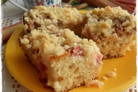 Szybkie ciasto jogurtowe z rabarbarem i kruszonką, podane na żółtym talerzyku. Idealne na letnie popołudnie.