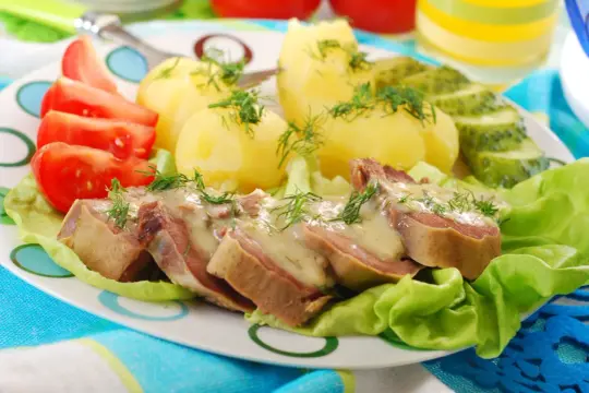 Pyszne ozorki w sosie chrzanowym, podane z ziemniakami, pomidorami i ogórkiem kiszonym.