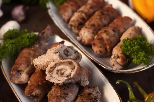 Roladki schabowe duszone w sosie własnym, z pieczarkami w środku, podane na dwóch półmiskach z natką pietruszki.