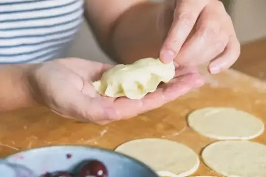 Dłonie formują pierogi. To tradycyjne polskie danie, które można nadziać owocami, serem lub mięsem.