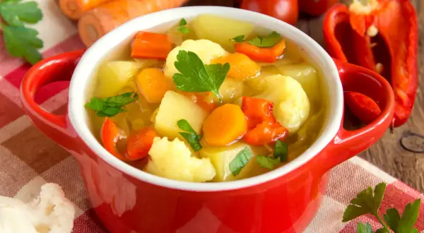 Aromatyczna zupa jarzynowa kcal, pełna warzyw: marchewki, ziemniaków, kalafiora i papryki, ozdobiona natką pietruszki.
