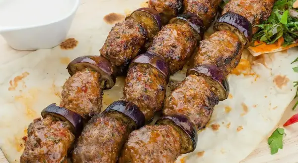 Kofta kebab z bakłażanem na płaskim chlebie, podany z sosem.