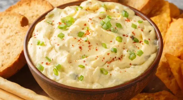 Kremowy dip z zieloną cebulką i papryką, otoczony chrupiącymi grzankami, nachos i paluszkami. Idealny do zanurzania!