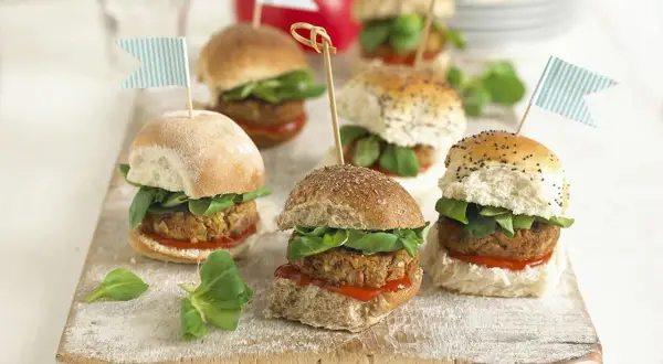 Mini burgery z kotletem, sałatą i flagietkami na desce.