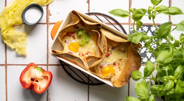 Pyszna tortilla na ciepło z piekarnika z jajkiem i serem, ozdobiona kolendrą. Obok papryka i bazylia.