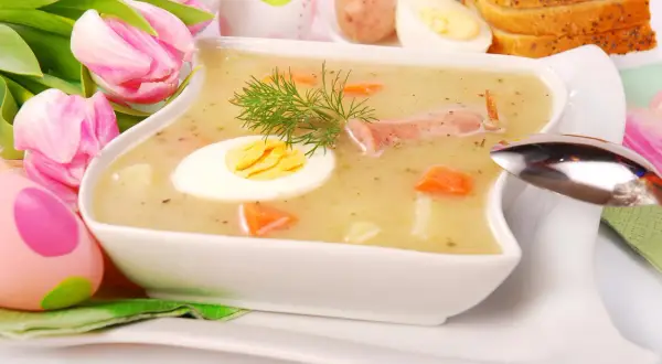 Biały barszcz przepis babci, z jajkiem i kiełbasą, ozdobiony koperkiem. W tle pisanki i tulipany.