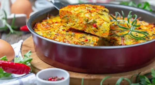 Pyszna, warzywna zapiekanka z jajek i warzyw, idealna na lekka kolacja. Podana z gałązką rozmarynu i papryczką chili.