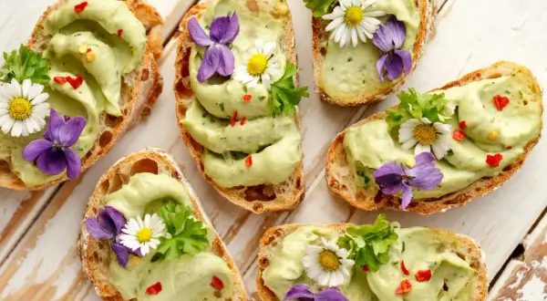 Pyszne **finger food**: grzanki z awokado, ozdobione kwiatami i ziołami. Idealne na wiosenne przyjęcie.