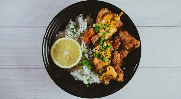 Chrupiące karaage z ryżem, polane sosem i posypane szczypiorkiem, z plasterkiem cytryny.