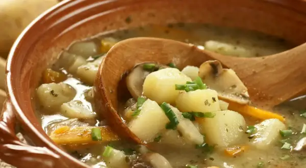 Zupa ziemniaczana przepis babci. Aromatyczna, domowa zupa z ziemniaków, marchewki i grzybów, podana w glinianej misce z drewnianą łyżką.