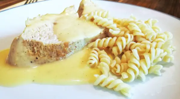 Kawałek pieczonego mięsa w kremowym sosie do potrawki, podany z makaronem fusilli.