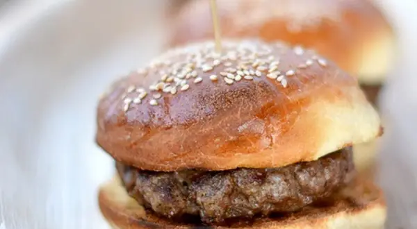 Mini burger z sezamową bułką i kotletem na talerzu.