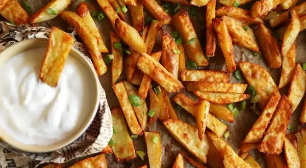Chrupiące frytki z piekarnika, posypane szczypiorkiem, zanurzane w sosie. Idealne, gdy chcesz wiedzieć, ile piec frytki w piekarniku, by były perfekcyjne.