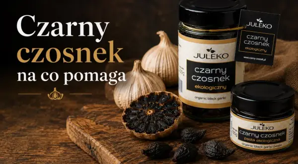 Czarny czosnek Juleko na desce. Słoiczki i ząbki czarnego czosnku, obok główki zwykłego czosnku.