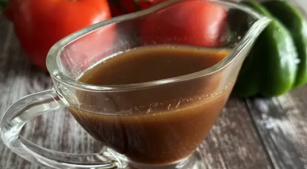 Sos balsamiczny w sosjerce, na tle pomidorów i zielonej papryki. Idealny do sałatek i mięs.