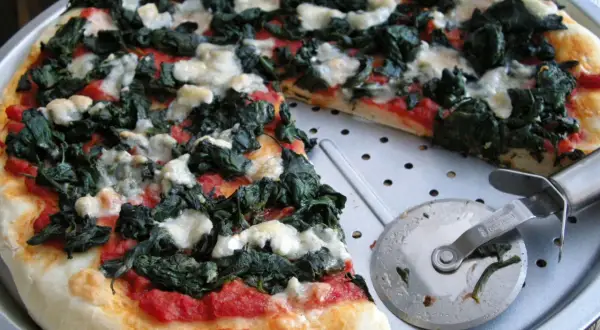 Pyszna pizza ze szpinakiem i białym serem, gotowa do pokrojenia.