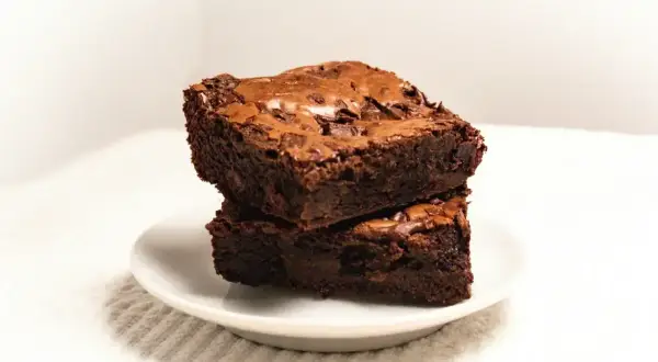 Dwa wilgotne kawałki ciasta brownie z płynną czekoladą, ułożone na białym talerzyku.