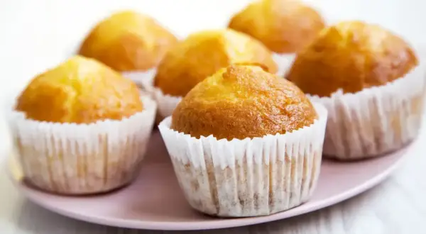 Idealny przepis na wilgotne i puszyste muffinki. Złociste, pachnące babeczki na różowym talerzyku.