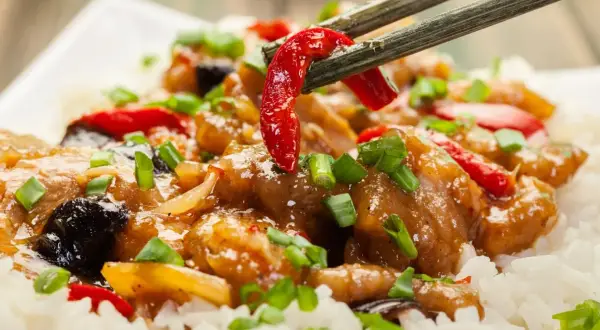 Schab po chińsku z ryżem, posypany szczypiorkiem. Pałeczki podnoszą kawałek papryczki chili z aromatycznego dania.