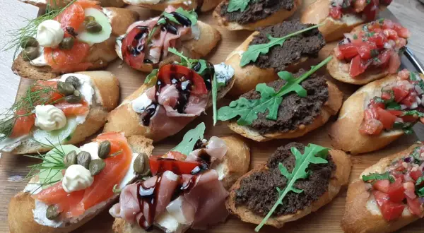 Tanie przekąski na imprezę: bruschetty z łososiem, szynką parmeńską, pastą z oliwek i pomidorami. Idealne na każdą okazję!