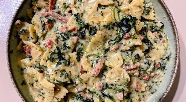 Pyszny makaron farfalle w kremowym sosie ze szpinakiem mrożonym i kawałkami boczku.