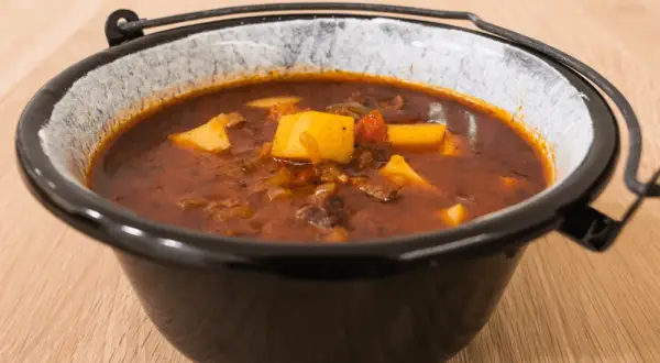 Gęsta, aromatyczna zupa gulaszowa przepis babci, z kawałkami mięsa i ziemniaków w głębokim, glinianym garnku.
