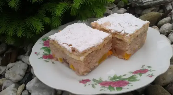 Dwa kawałki ciasta z kisielem na oleju, posypane cukrem pudrem, na talerzyku z różami, wśród kamieni i gałązek choinki.