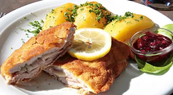 Pyszny kotlet po szwajcarsku, podany z ziemniakami, plasterkiem cytryny i żurawiną.