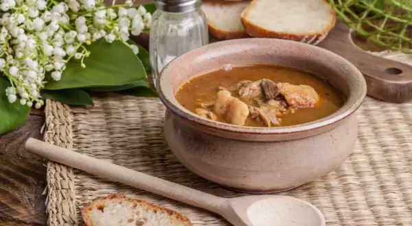 A rustic bowl brimming with the najlepsza zupa gulaszowa, accompanied by crusty bread slices and a wooden spoon.