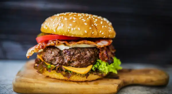 Soczysty burger z wołowiny z bekonem, serem, pomidorem i sałatą na desce.