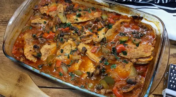 Schab po cygańsku z pieczarkami i papryką w sosie pomidorowym, posypany natką pietruszki, w szklanym naczyniu żaroodpornym.