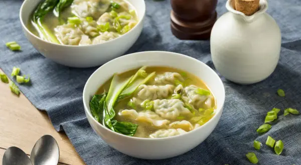Dwie miseczki aromatycznej zupy won ton z zielonymi warzywami i posiekanym szczypiorkiem.