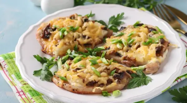 Schab w plastrach pieczony w piekarniku z pieczarkami i serem, posypany szczypiorkiem.
